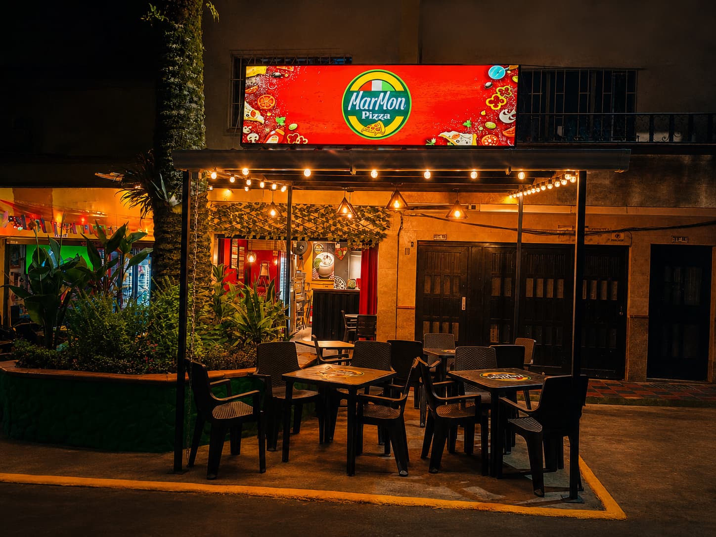 Fachada del local MarMon Pizza en Envigado de noche con luces cálidas y mesas al aire libre